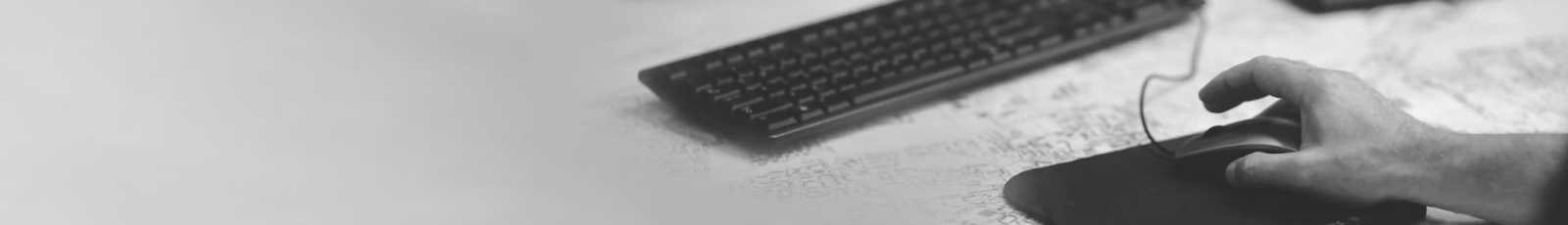 Graustufenbild einer Hand an einer Mouse vor einer Tastatur